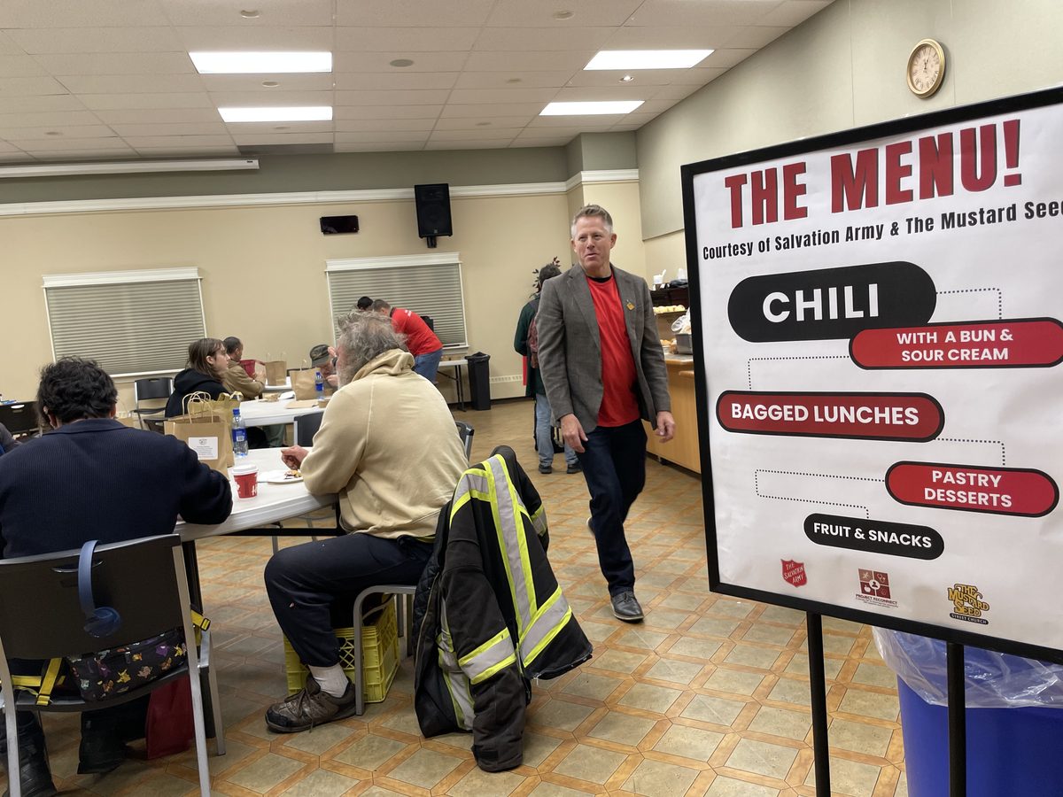 Attendees sharing a hot meal beside the day's menu board, courtesy of the Salvation Army and The Mustard Seed